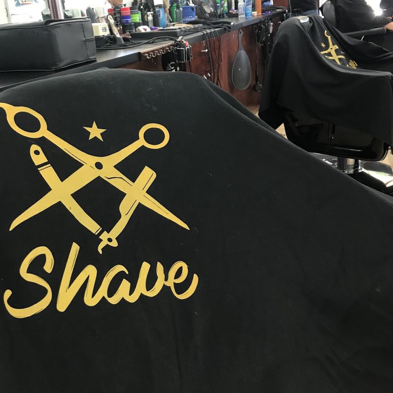 Capa de Shave Barbershop con el logo de tijeras doradas