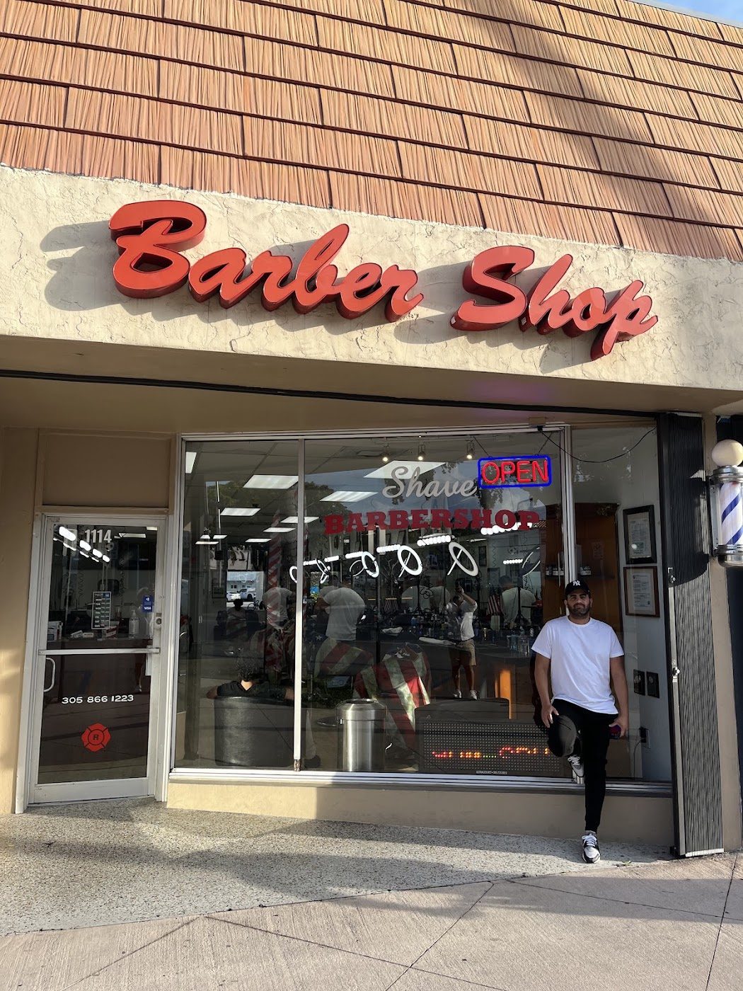 Fachada de Shave Barbershop en Normandy Drive, Miami Beach — letrero rojo en cursiva sobre la puerta de cristal